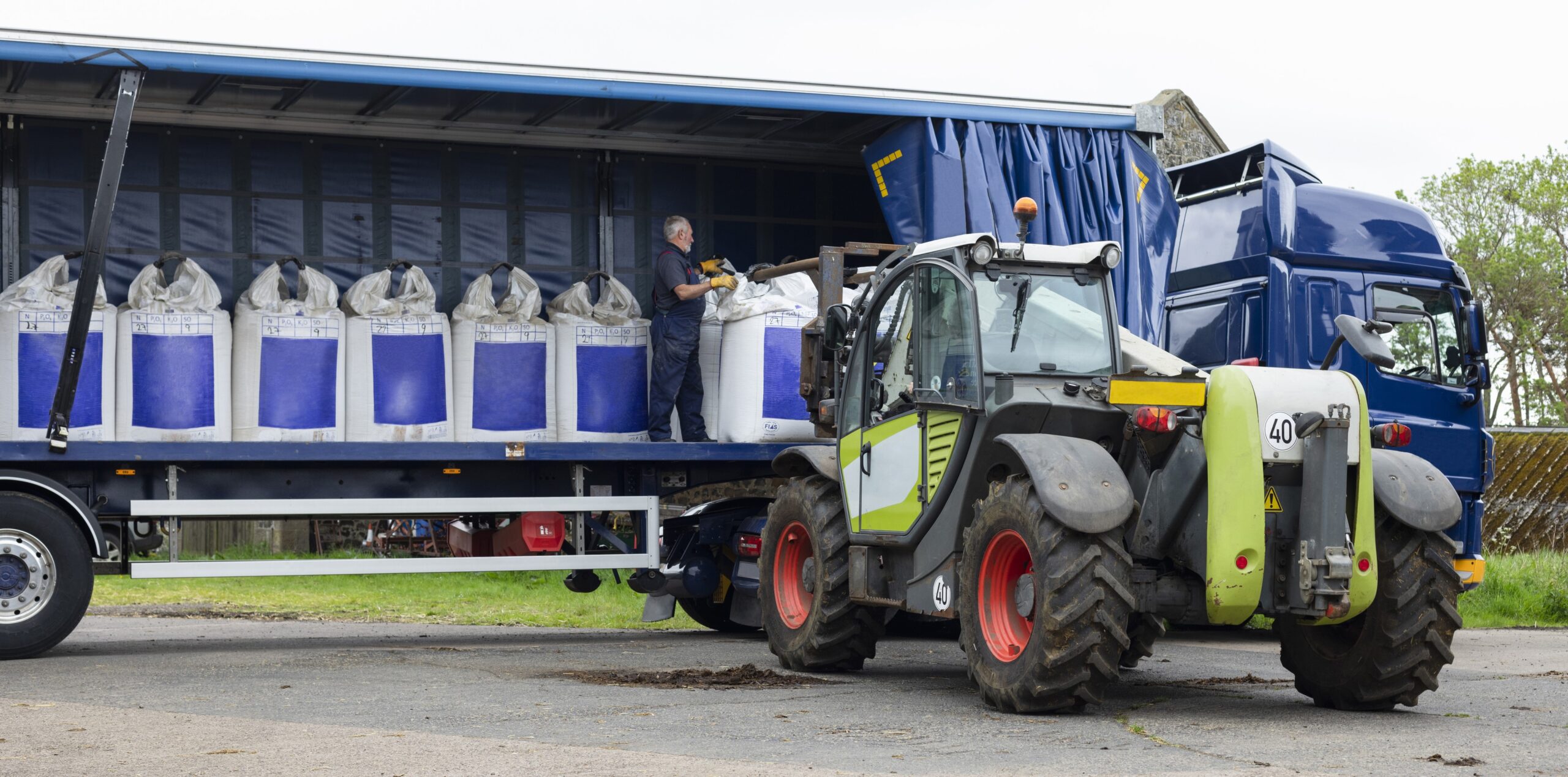 An employee taking farm loads off a lorry using a telehandler truck