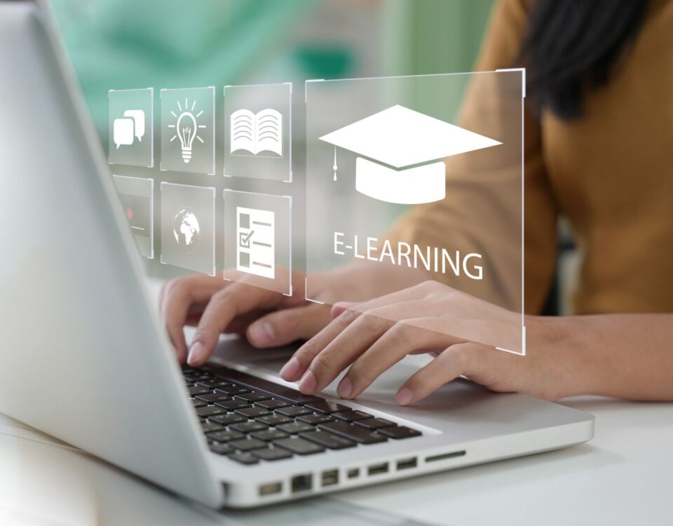 Individual typing on a laptop with e-learning icons displayed on the screen.