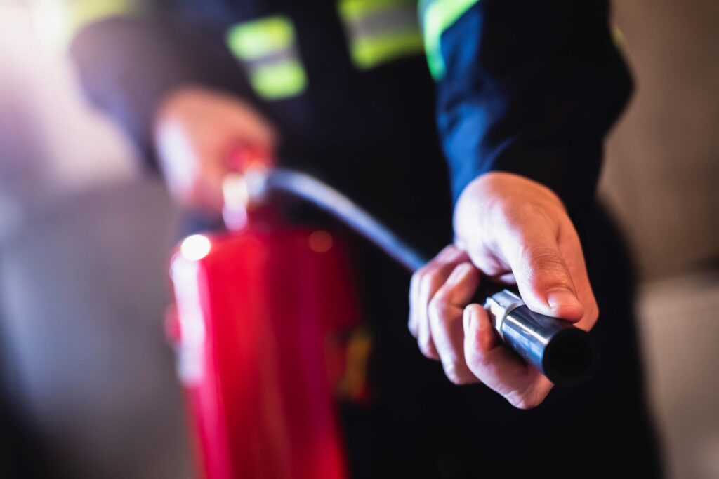 A worker in dark clothing holds a red fire extinguisher and grips the nozzle during fire extinguisher training.