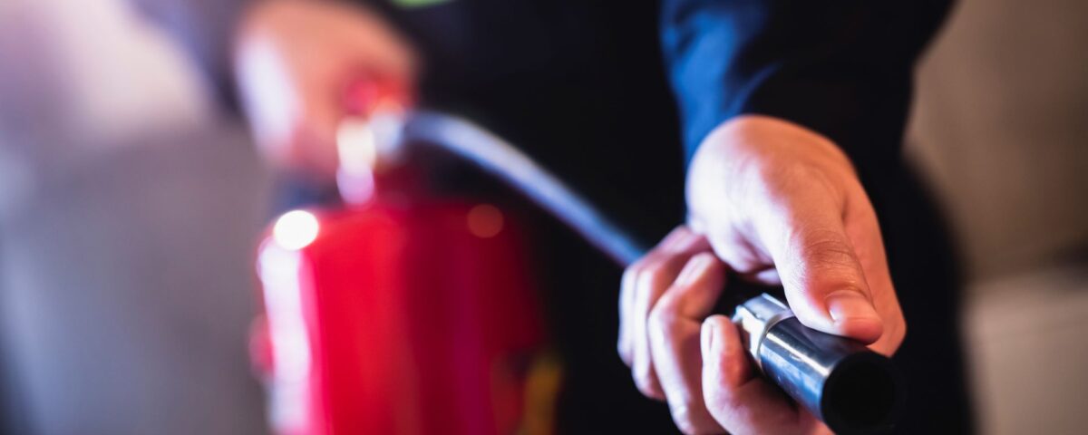 A worker in dark clothing holds a red fire extinguisher and grips the nozzle during fire extinguisher training.