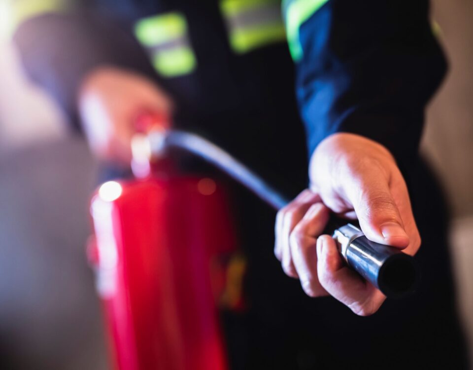 A worker in dark clothing holds a red fire extinguisher and grips the nozzle during fire extinguisher training.