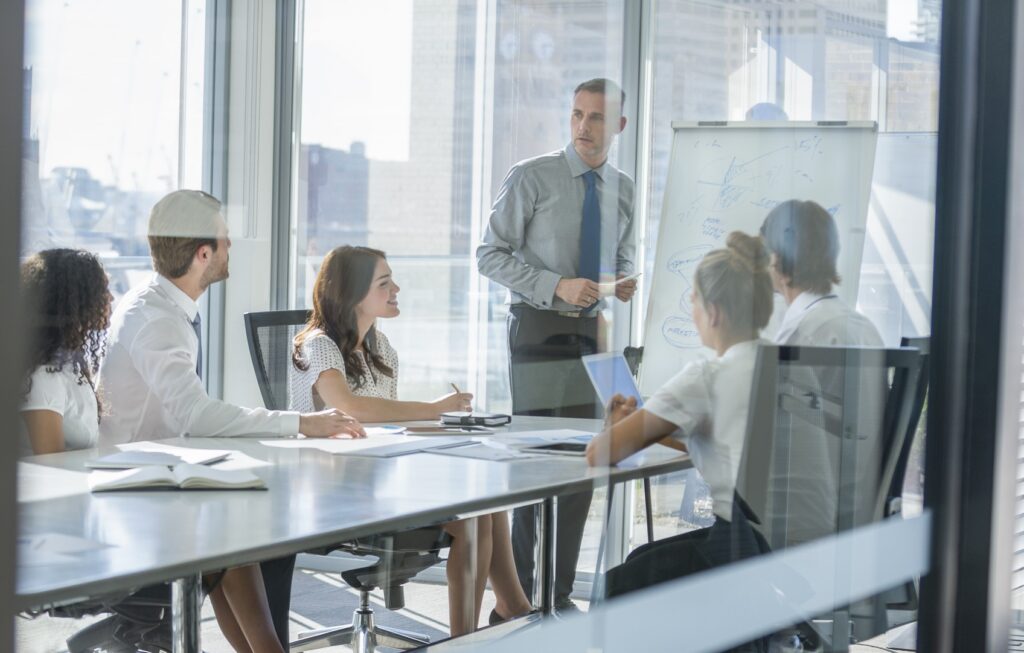 A trainer speaks to a small team during an IOSH working safely session in a glass-walled office meeting room.