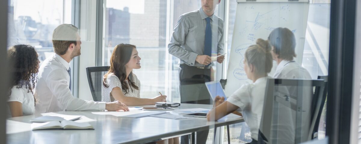 A trainer speaks to a small team during an IOSH working safely session in a glass-walled office meeting room.