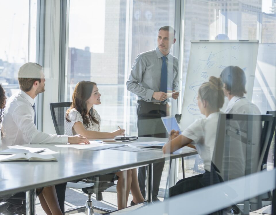 A trainer speaks to a small team during an IOSH working safely session in a glass-walled office meeting room.
