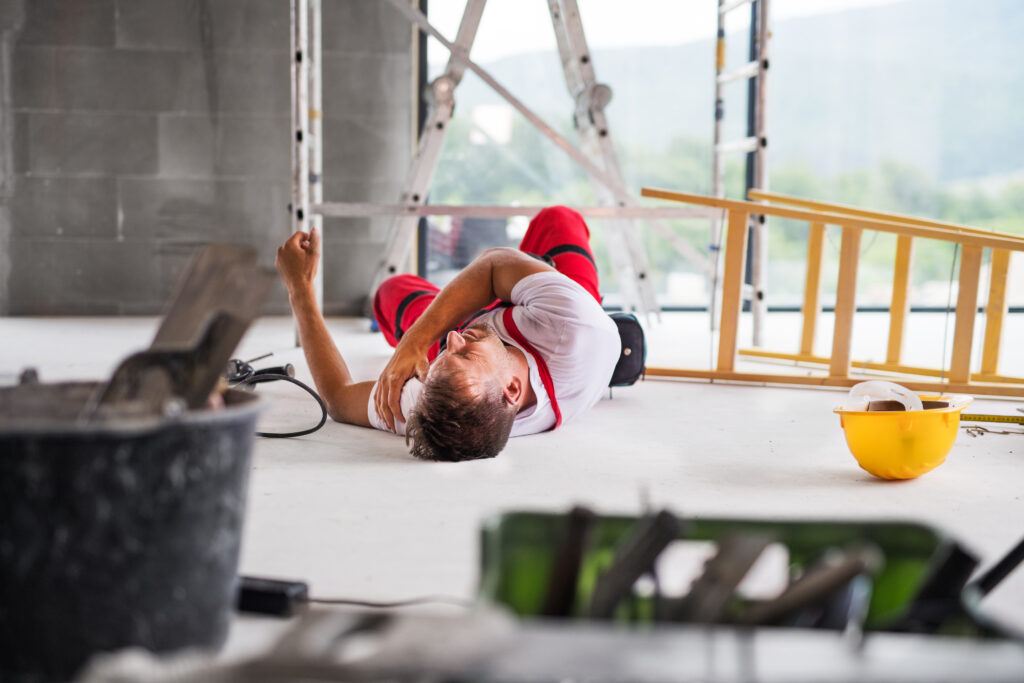 Construction worker lying on the floor with an injured arm in a building site environment.