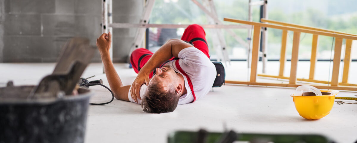 Construction worker lying on the floor with an injured arm in a building site environment.