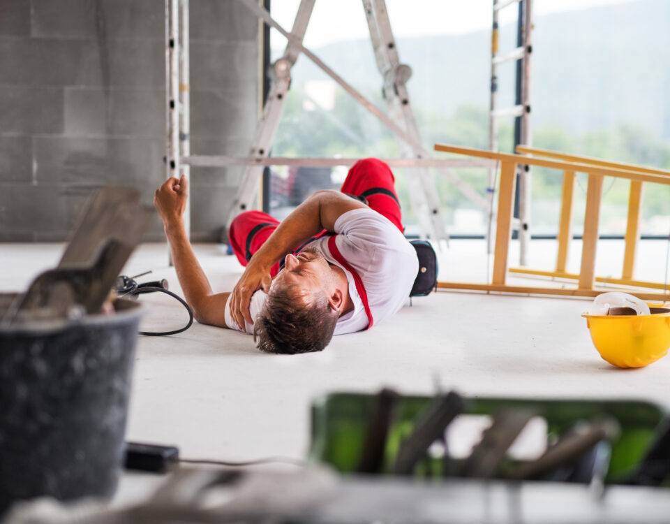 Construction worker lying on the floor with an injured arm in a building site environment.