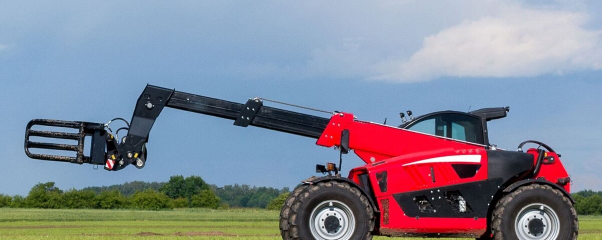 A red telehandler rests on grass with its boom extended leftward beneath a dramatic cloudy sky.