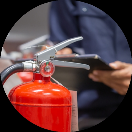 A red fire extinguisher stands in the foreground while a person in a dark uniform holds a clipboard during a safety check.