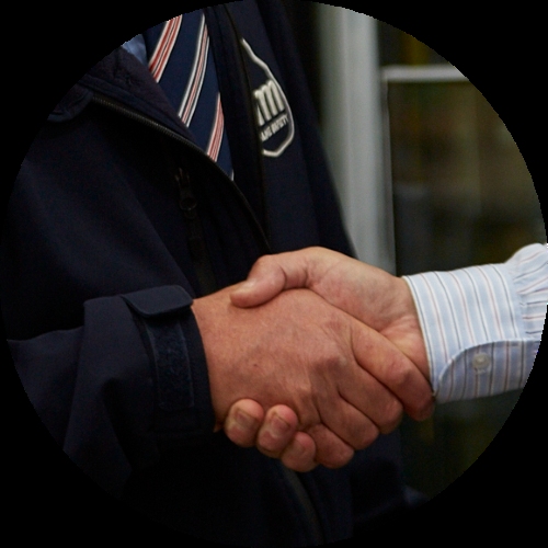Two people shake hands, one wearing a dark jacket and striped shirt, in a close-up business greeting.