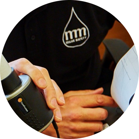 A hand holds a lung function testing device beside a person wearing a black shirt with an mm logo during a health check.